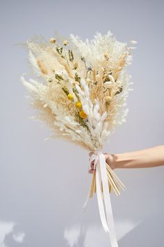 a bouquet of dried flowers being held by someone's hand on a gray background