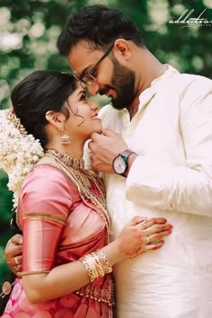 a man and woman standing next to each other in front of some trees with flowers