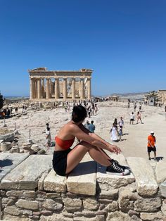 a woman sitting on top of a stone wall in front of an ancient building with columns