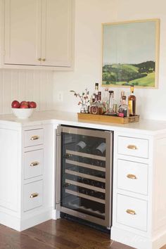 a wine rack in the corner of a kitchen with white cabinets and wood flooring