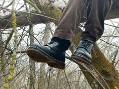 a person wearing black shoes standing on a tree branch in the middle of a forest