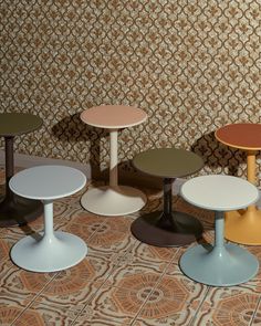 four different colored tables sitting next to each other on a tiled floor in front of a wall