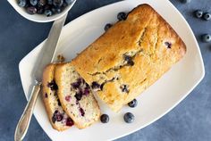 a loaf of blueberry bread on a plate next to a bowl of blueberries