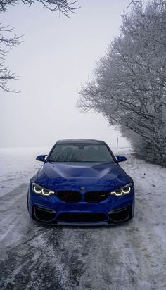 a blue car parked in the middle of a snow covered road next to some trees