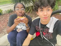 two young people sitting on a bench eating food