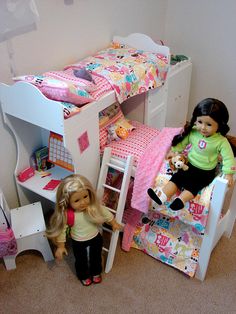 two dolls are sitting on the floor next to a bunk bed with a desk and chair