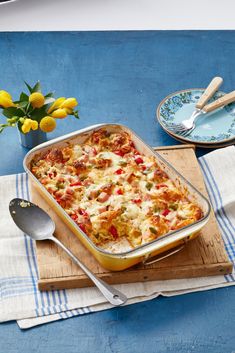 a casserole dish with vegetables and cheese on a wooden board next to flowers