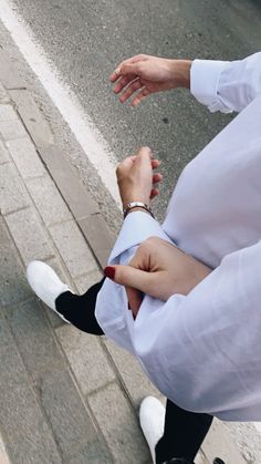 a person in white shirt and black pants standing on the street with their hands together