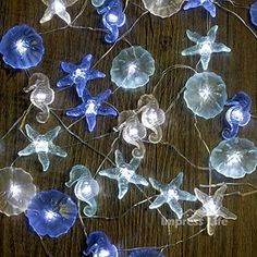 blue and white glass flowers are arranged on a wooden table with string lights in the middle