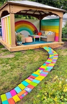 a colorful rainbow painted pathway leading to a wooden gazebo in a backyard with chairs and tables