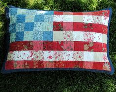 a red, white and blue patchwork pillow laying on the grass