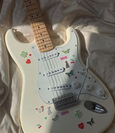 a white electric guitar with stickers on it's body sitting on a sheet