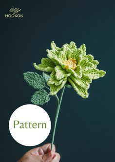 a crocheted green flower with leaves is shown in front of a dark background