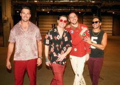 three men standing next to each other in front of a warehouse door wearing red pants and sunglasses