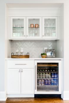 a kitchen with white cabinets and an open wine cooler in the center, filled with drinks