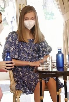 a woman sitting at a table wearing a face mask and holding a blue cup in front of her