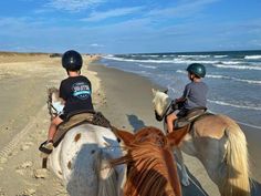 two people riding horses on the beach next to the ocean with waves in the background