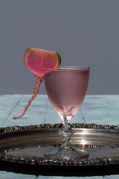 a pink drink sitting on top of a metal tray next to a slice of radish