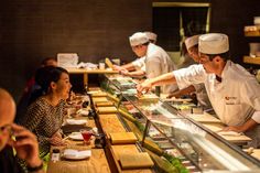 a group of people sitting at a table with sushi in front of the counter