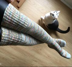 a cat sitting on the floor next to a woman's legs with colorful socks