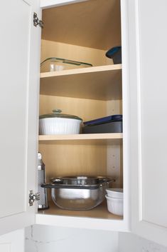 an open cabinet with pots and pans on the bottom shelf, including one bowl