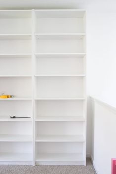 an empty white bookcase in the corner of a room with carpeted flooring