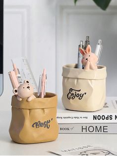 two ceramic pen holders with pens and pencils in them on top of a desk