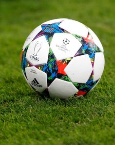 a soccer ball sitting on top of a lush green field with white and red designs