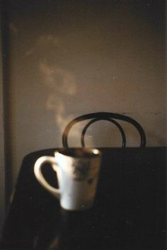 a coffee cup sitting on top of a black table next to a suitcase and shadow