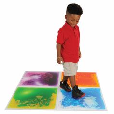 a young boy standing in front of an art project on the ground with colored paper