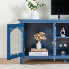 a blue cabinet with books, vase and flowers on it in front of a flat screen tv