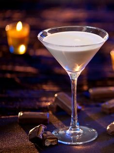 a glass filled with white liquid sitting on top of a table next to chocolate pieces