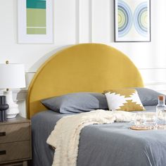 a yellow headboard on a bed in a room with white walls and pictures above it