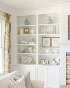 a living room filled with white furniture and lots of bookshelves above a fire place