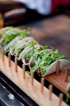 several burritos with lettuce and tomatoes on a wooden tray lined up