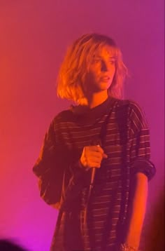 a woman holding a microphone in front of a purple and pink background with light coming from behind her