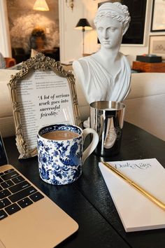 a laptop computer sitting on top of a desk next to a statue and cup filled with coffee