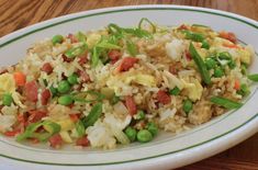 rice with peas and other vegetables on a white plate sitting on a wooden table top