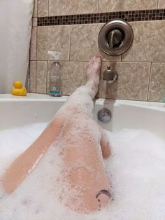 a person laying in a bathtub with foam on their legs and feet, next to a shower head