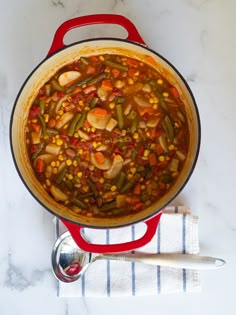 a red pot filled with vegetables on top of a white counter next to a spoon