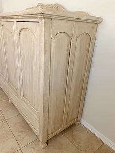 a white cabinet sitting in the corner of a room next to a wall and tiled floor