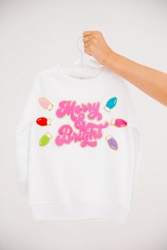 Get your little ones in the festive spirit with our MINI KIDS MERRY & BRIGHT WHITE PULLOVER. This white pullover features a playful pink Merry & Bright patch and festive christmas lights patches. Perfect for adding a touch of holiday cheer to their outfit! All orders are currently shipping within 14 business days. To receive item quicker, expedited shipping is available at checkout. **All Christmas orders must be placed with expedited shipping to guarantee delivery by Dec. 24 if placed after Dec Cute White Holiday Tops, Festive Pink Crew Neck Top, White Festive Holiday Sweater, White Holiday Festive Sweater, Pink Holiday Festive Tops, Pink Holiday Festive Top, Pink Holiday Tops For Festive Occasion, Cute White Top For Festive Occasions, Cute White Christmas Sweatshirt