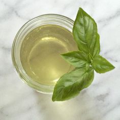 a glass cup filled with green tea on top of a marble counter next to a leaf