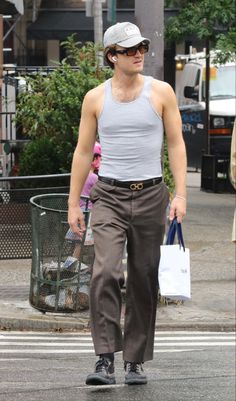 a man walking across a street holding a shopping bag and wearing sunglasses on top of his head