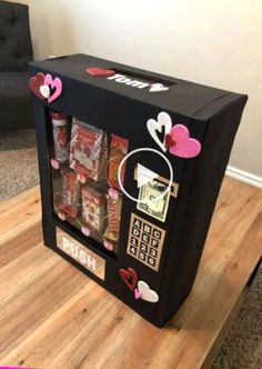 a small vending machine with hearts on it's side and some candy in the middle