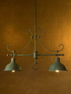 three light chandelier hanging from the ceiling in front of a brown brick wall