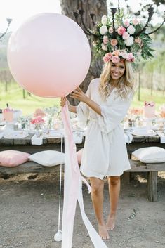 a woman holding a large pink balloon in front of a table with flowers on it