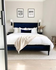 a bed with white sheets and pillows in a bedroom next to two pictures on the wall