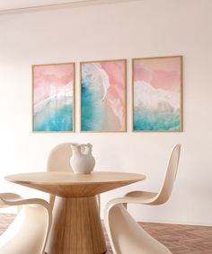 two paintings hang on the wall above a round table with white chairs and a vase