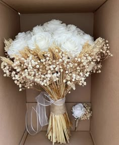 a bouquet of white roses in a cardboard box with some ribbon on the side and a bow tied around it